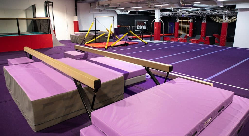 Flexible gymnastics flooring and trampoline area in an indoor gymnasium with colourful padded equipment and obstacle courses for indoor gymnastics training.