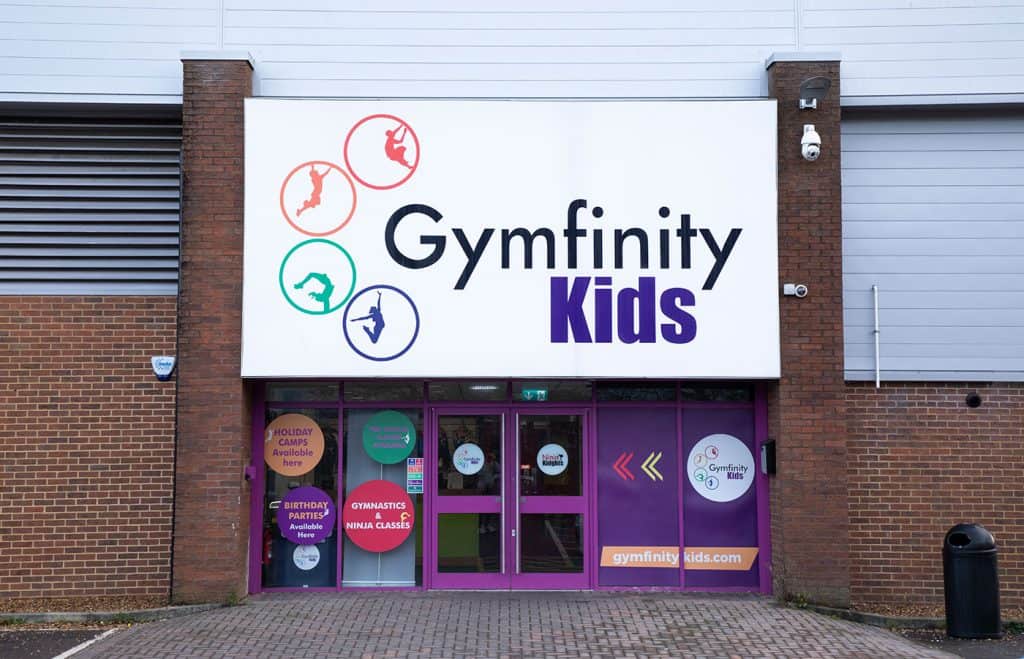 Flexible and colourful signage for Gymfinity Kids, a children's gym specialising in gymnastics and ninja classes, with promotional posters on the entrance doors.