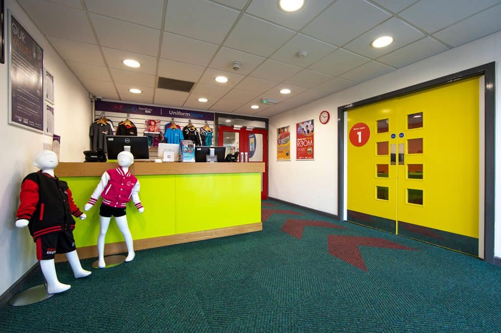 Uniform store reception area with mannequins dressed in sportswear and a bright yellow door; a family-friendly athletic apparel shop with colourful displays and signage.
