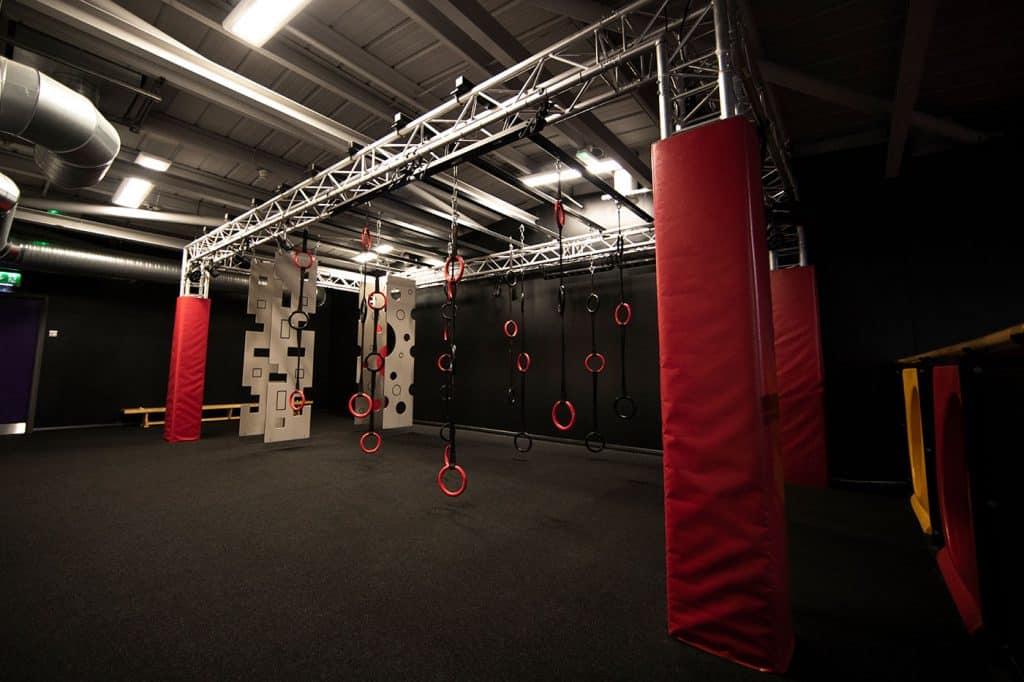 Climbing training area with rings, ledges, and padded columns in an indoor fitness centre. Suitable for obstacle course practices and advanced fitness training exercises.