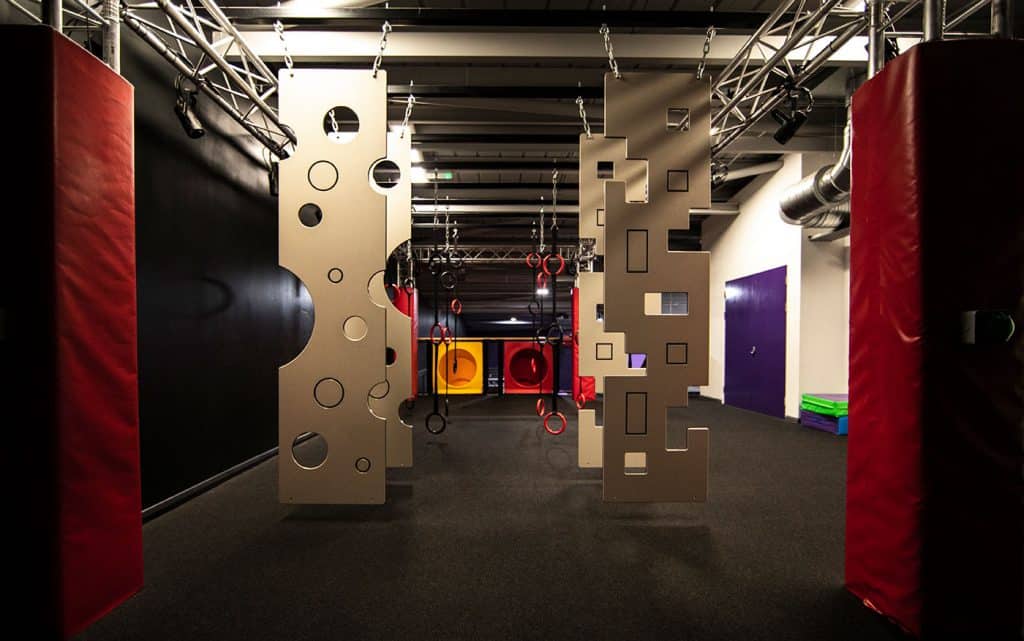 Climbing gym with foam padded walls and obstacle course, featuring hanging gymnastic rings and various climbing structures for fitness and training.