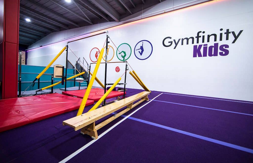 Flexible gymnastics equipment for kids in a colourful indoor sports facility, featuring padded mats, climbing frames, and a balance beam for active play and development.