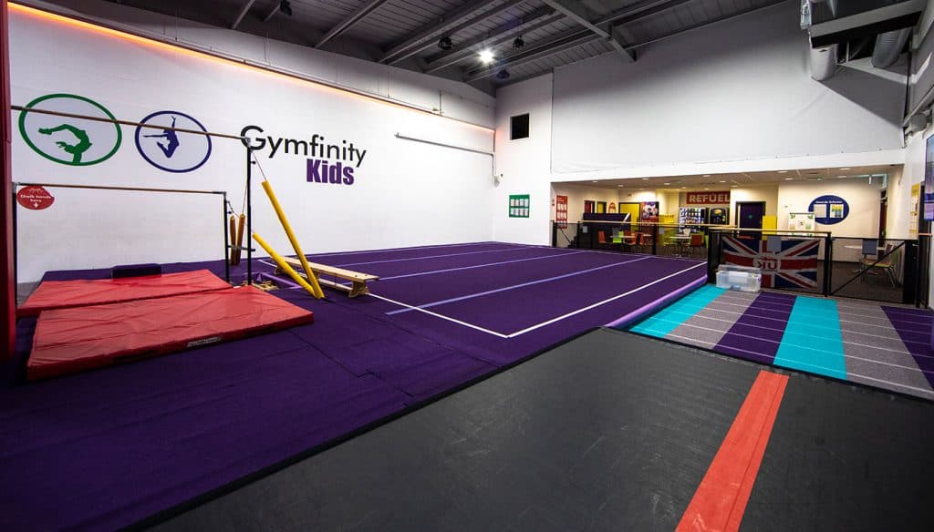 Bright indoor gymnastic training area for children with purple mats and wall graphics at Gymfinity Kids, featuring equipment for gymnastics practice and activities.