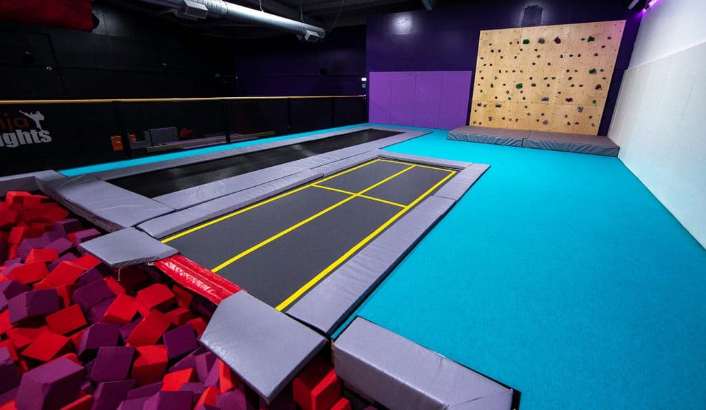 Colourful indoor trampoline park with padded safety barriers, a foam pit, and a climbing wall for kids and adults to enjoy active fun and physical exercise.