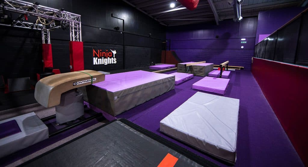 Flexible Ninja Warrior obstacle course with padded mats and climbing elements in a dark, vibrant training facility.