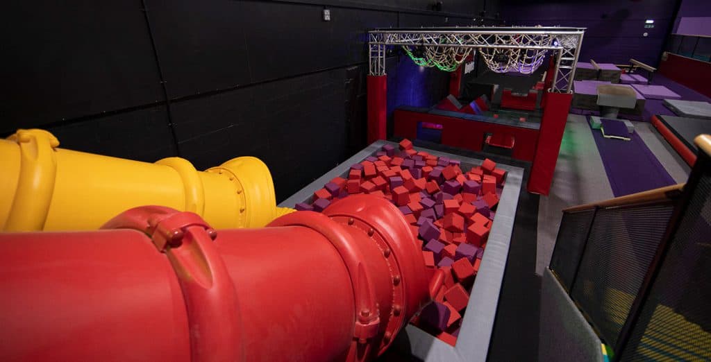Vivid indoor trampoline park with colourful foam pit, large red and yellow slide, and climbing ropes for kids and adults to enjoy active fun.