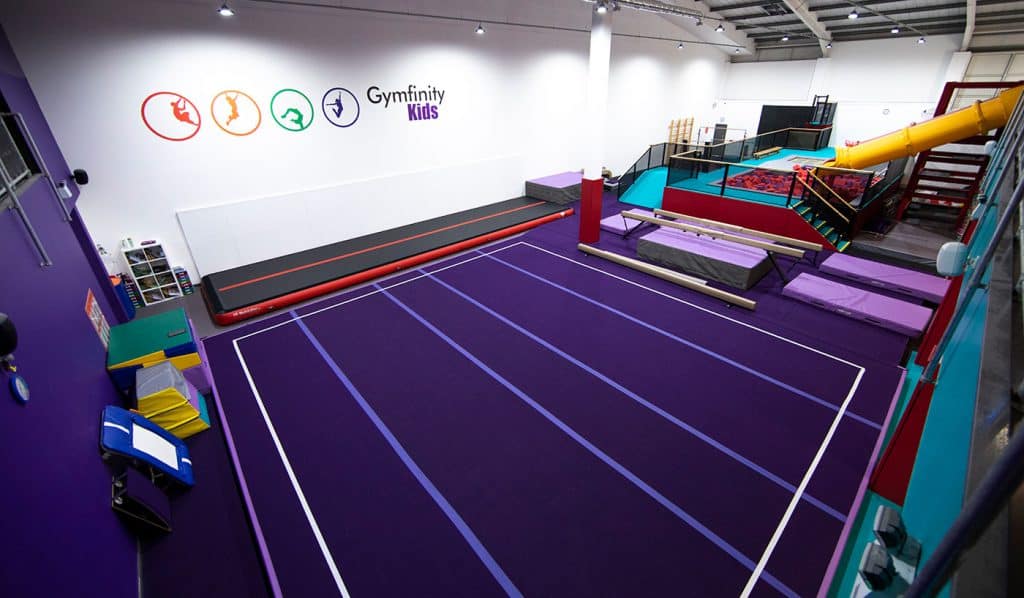 Brightly coloured indoor gymnastic facility for kids, featuring foam pits, trampoline area, climbing frames, and a variety of sports equipment for children's physical activities.