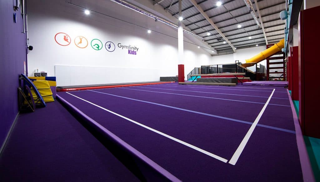Bright indoor gymnastic training area with purple mats, climbing equipment, and a slide, part of Gymfinity Kids' dedicated facility for children’s gymnastics and physical development.