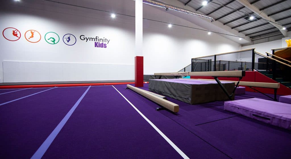 Jumping various gymnastic tricks on mats at Gymfinity Kids indoor sports centre. The facility features padded floors, gymnastics equipment, and a vibrant environment for children's fitness activities.