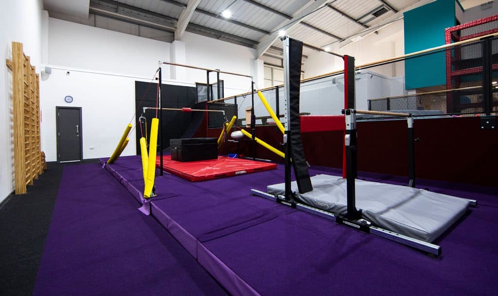 Obstacle courses with padded mats and safety rails inside a gymnastics or training facility.