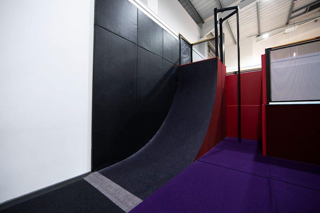 Blake's indoor skateboarding ramp with black, red and purple padding and safety barriers in a modern sports facility.