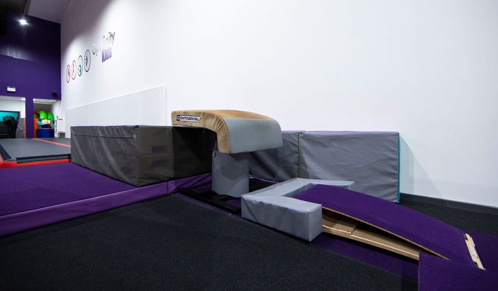 Soft play area with gymnastics equipment, including a springboard, padded mats, and foam blocks, suitable for children's activities and physical development in an indoor gymnastics or activity centre.