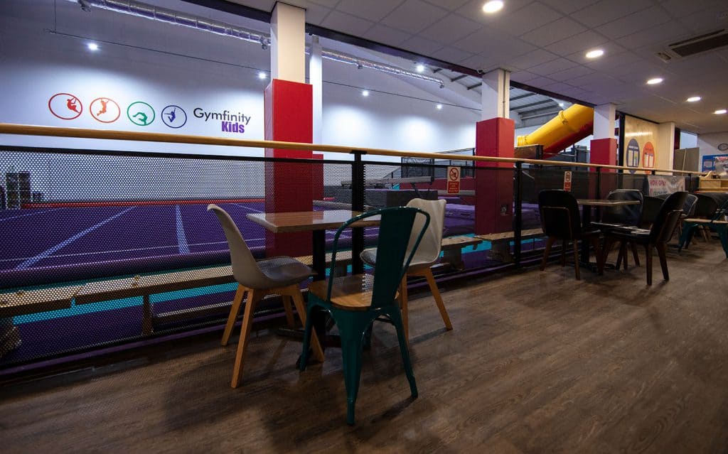 Indoor view of a children's gymnastics area with colourful equipment, seating and a safety barrier in a recreational centre.
