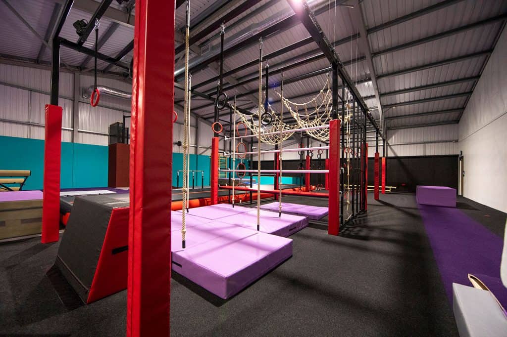 Vibrant indoor ninja warrior obstacle course with padded mats, ropes, and climbing frames for kids’ active play and fitness. Perfect for children’s parties and adventure challenges.