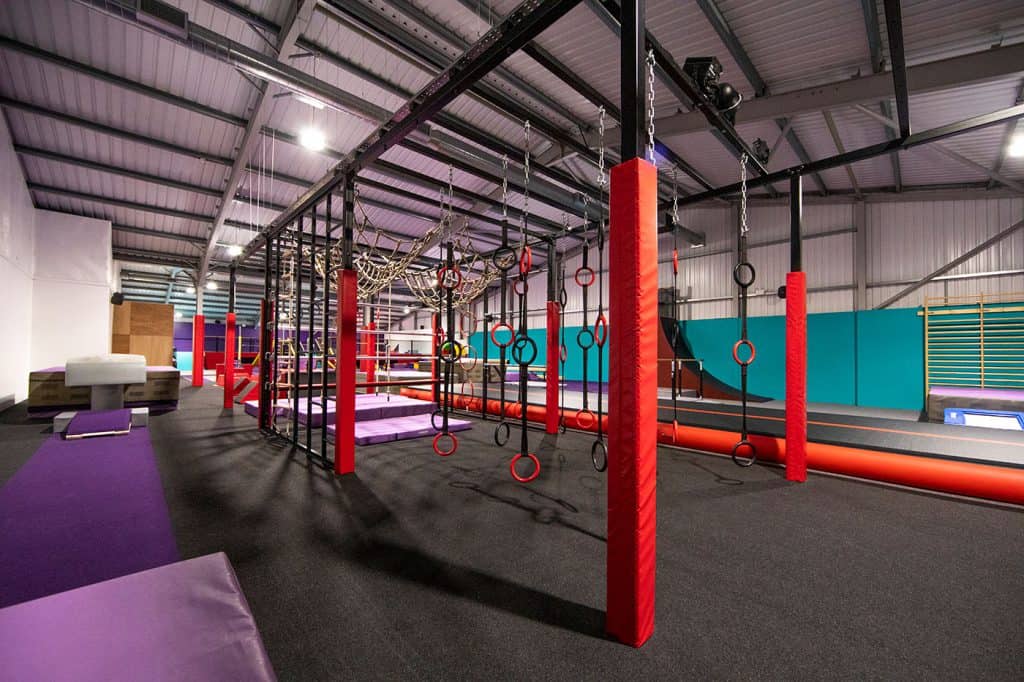 Bright indoor adventure playground featuring climbing frames, gymnastic rings, and padded areas for children’s fun and activity. Suitable for kids' sports and physical development.