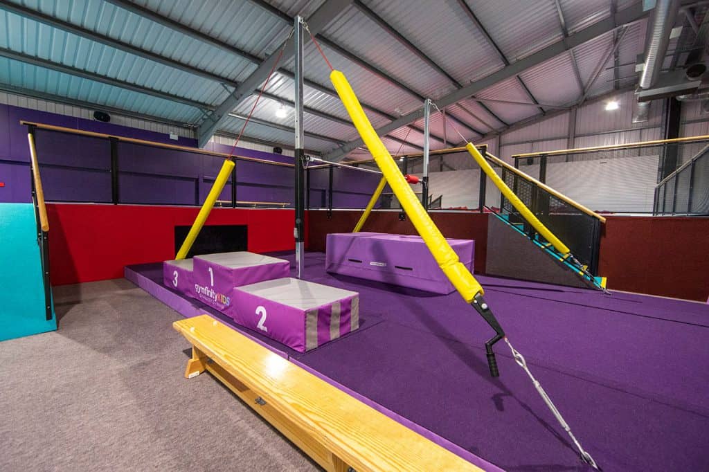 Suspension training apparatus inside kids' indoor play area with purple and red colour scheme and soft padding.