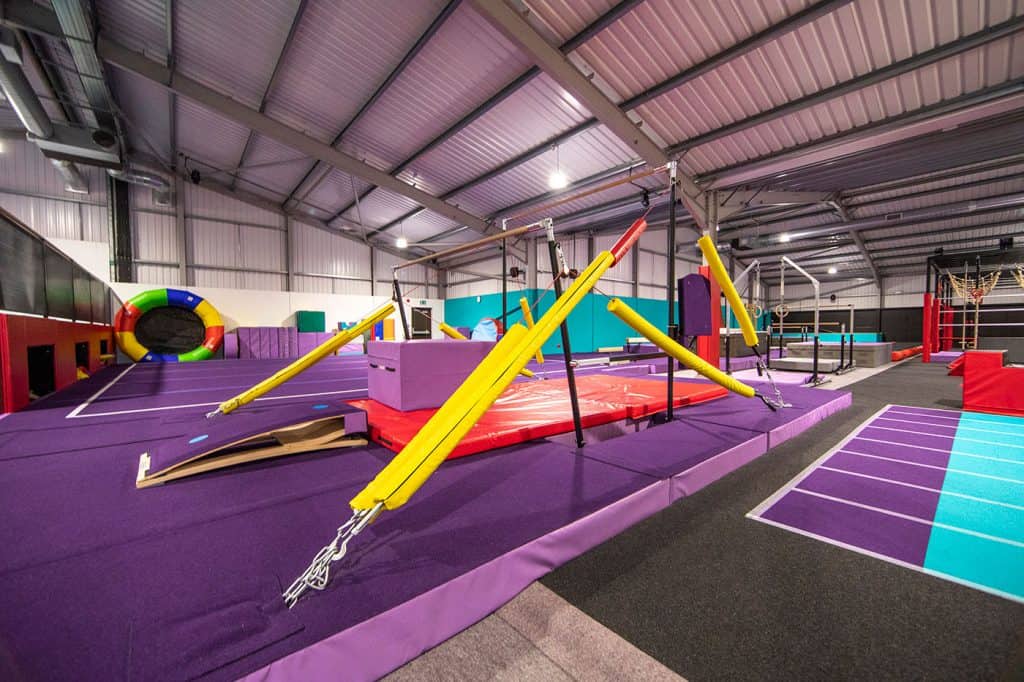 Colourful indoor gymnastics and obstacle course equipment in a spacious gymnasium.