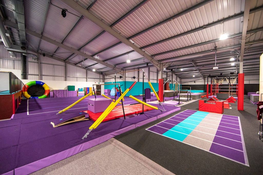 Jumping training and obstacle course in an indoor trampoline park with soft mats and colourful equipment for kids and adults to enjoy active play and exercise in a spacious, well-lit environment.