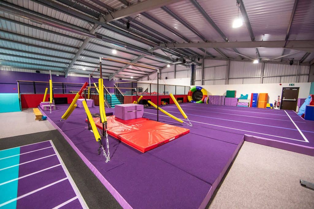 Vibrant indoor trampoline park featuring purple padded flooring, safety nets, and various bouncing areas for kids and adults to enjoy active play and physical exercise.