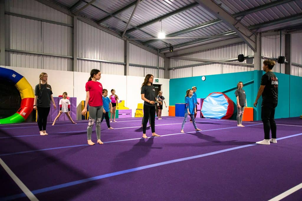 Ballet-training-class-in-indoors-gymnasium-with-children-practicing-dance-on-purple-matted-floor.