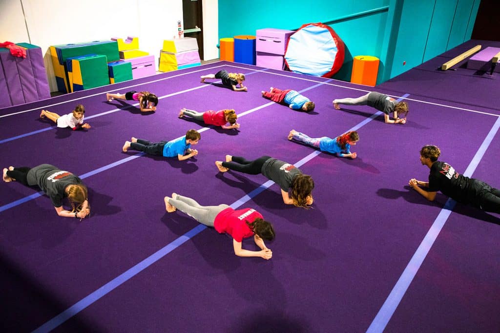 Childrens gymnastics class practising plank exercise on purple mat in indoor activity centre.