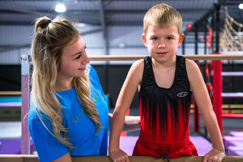 Teenage girl helping young boy in gymnastics training at indoor gym.