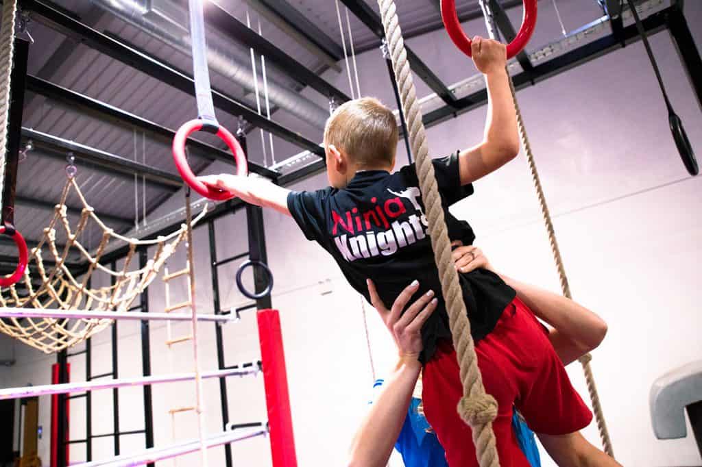 Climbing and gymnastic training for kids at Ninja Knights indoor obstacle course. Child participating in strength and agility exercises under adult supervision.