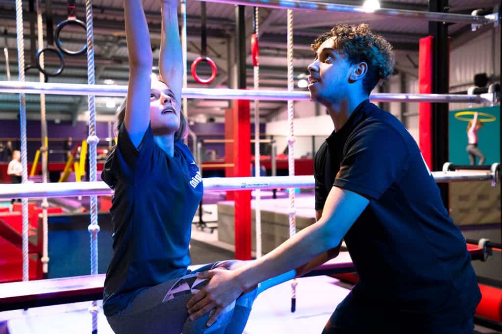 Climbing trainer assisting young girl on indoor fitness ropes in a modern gym.