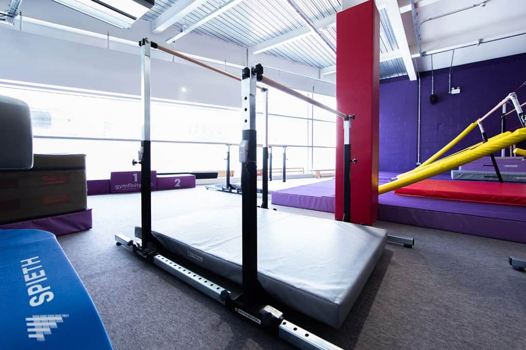 Gymnfinity gymnastics training area with mats and bars for tumbling and conditioning, bright indoor space with large windows, suitable for gymnastics practice and training.