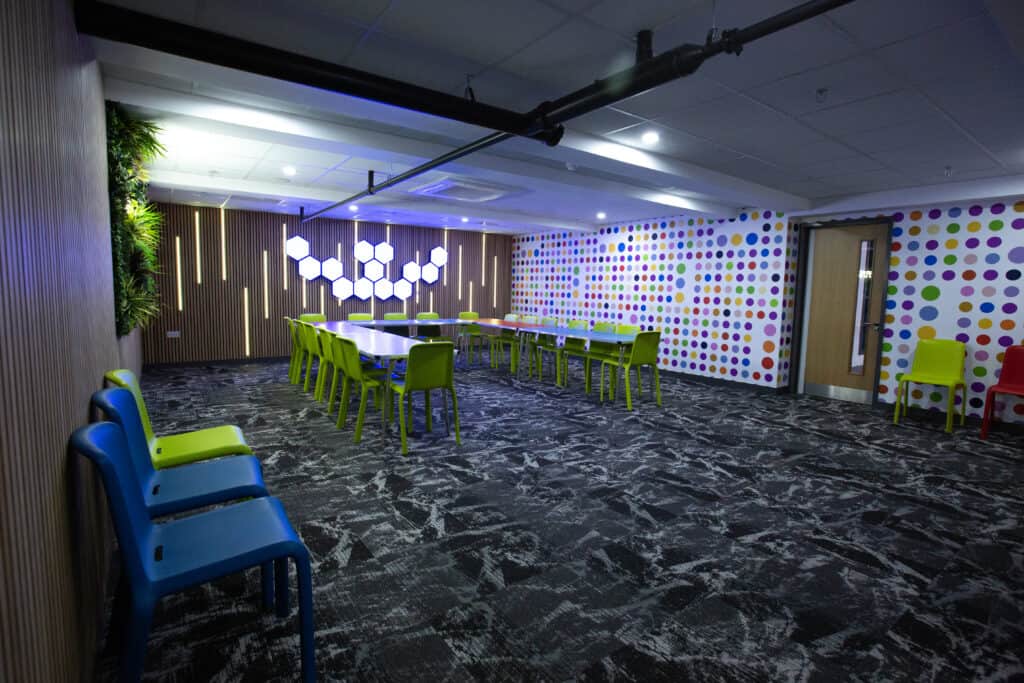 Colorful conference room with lime green chairs, polka dot wall design, and modern lighting fixtures, ideal for meetings and collaborative events.