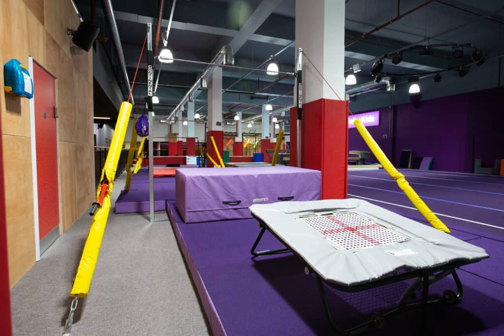 A vibrant indoor trampoline park featuring purple padded flooring, safety barriers, and various trampoline zones for recreational bouncing and jumping activities.