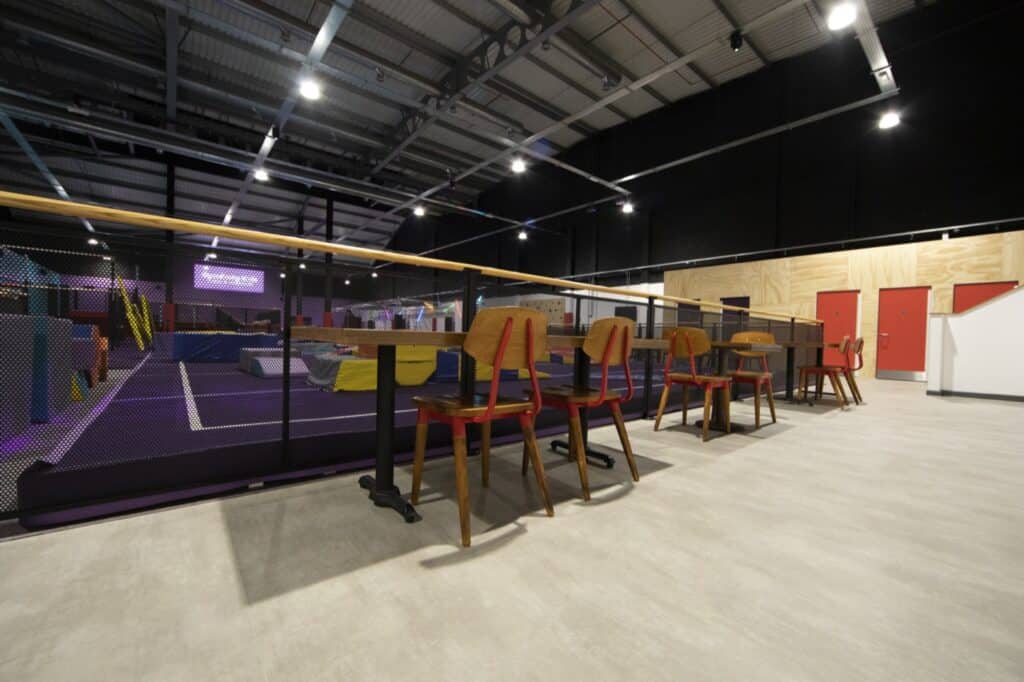 Climbing gym with viewing area, wooden chairs and safety netting, indoor recreational facility, modern sports arena, fitness and entertainment centre in warehouse setting.
