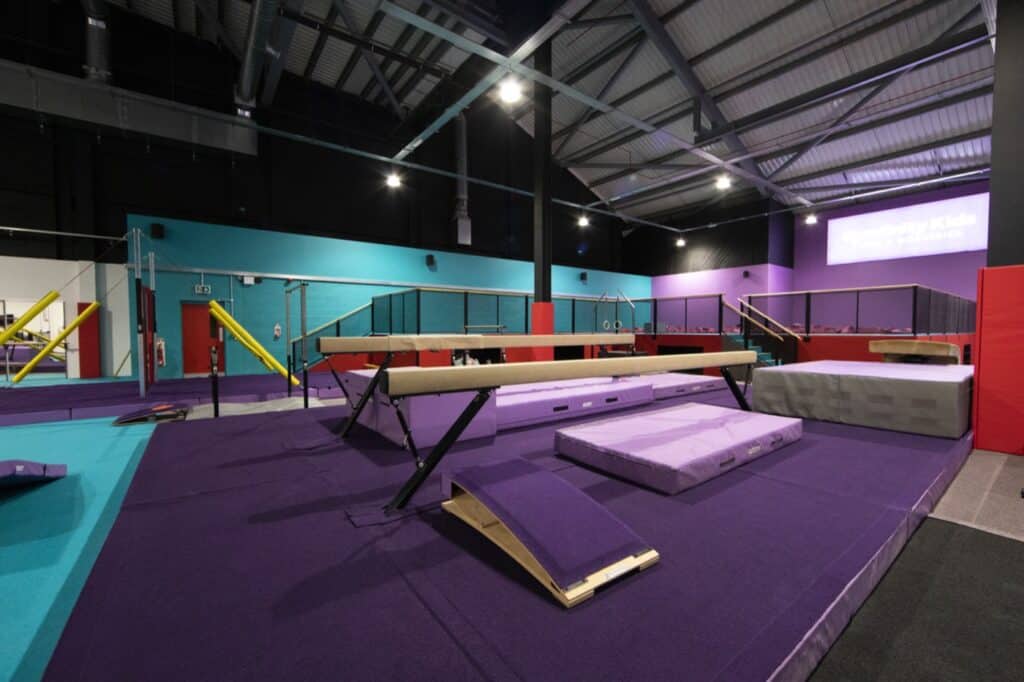 Flexible gymnastics training area with various mats, beams, and bars inside a colourful indoor sports facility.
