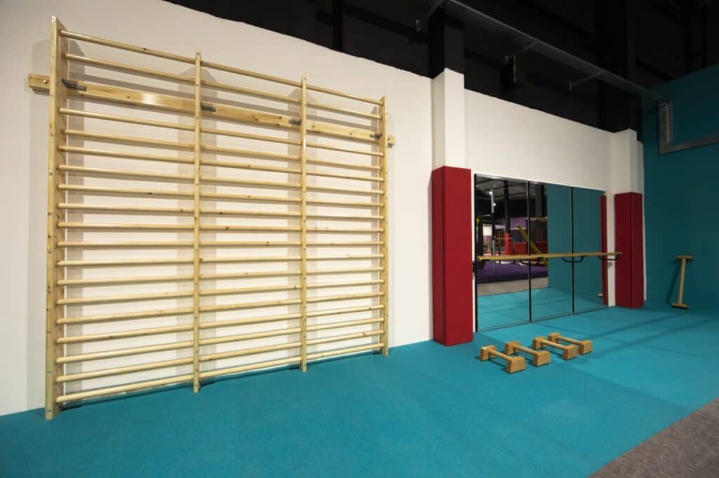 Climbing wall and gymnastics training area with wooden bars and padded floor in a modern fitness gym.