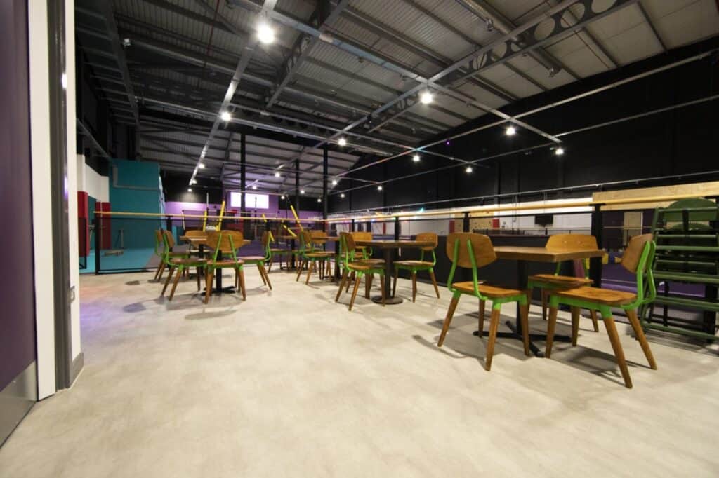 Modern indoor recreational area with wooden chairs and tables, illuminated by ceiling lights, featuring a vibrant and spacious layout suitable for social gatherings and activities.