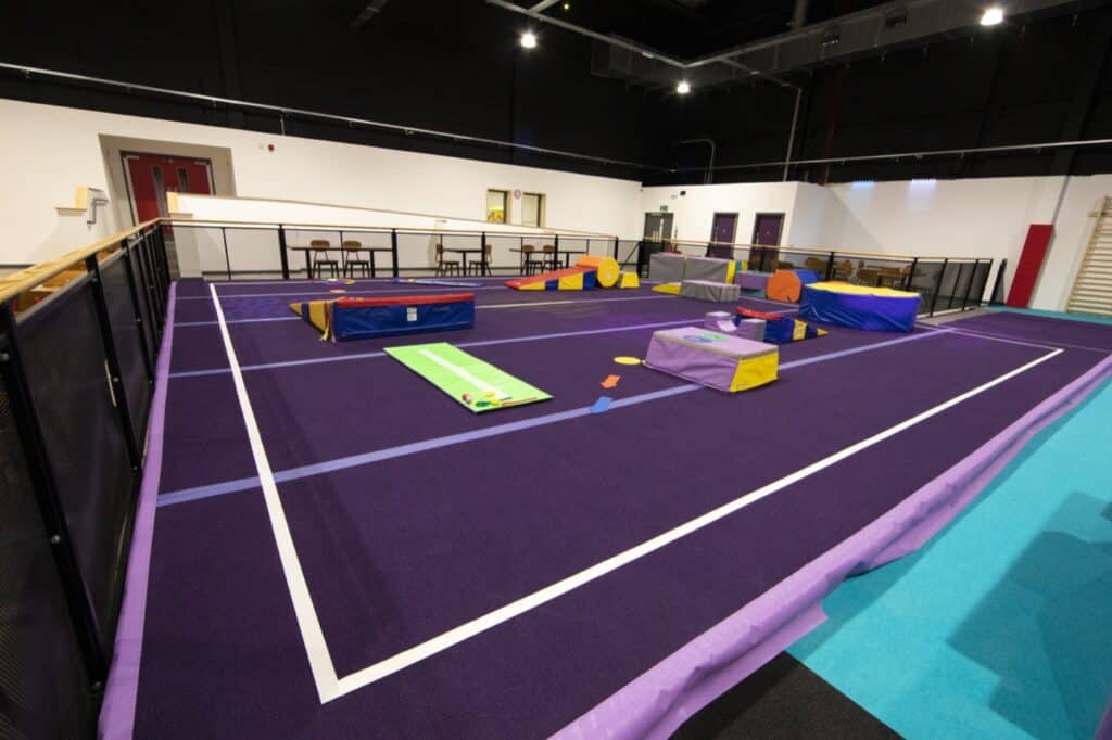 Bright indoor gymnasium with colourful soft play equipment and agility obstacles for children's activities or physical therapy. Spacious with safety features including padded flooring and barriers.