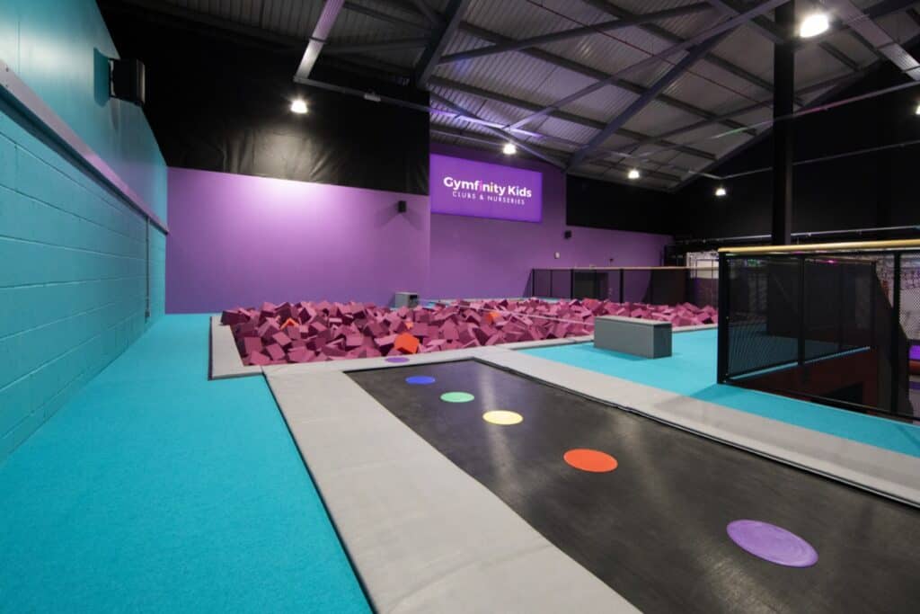 Soft play area at Gymfinity Kids with foam pits and trampolines, vibrant coloured walls and safety padding, ideal for children's fitness and recreational activities within a modern indoor sports facility.