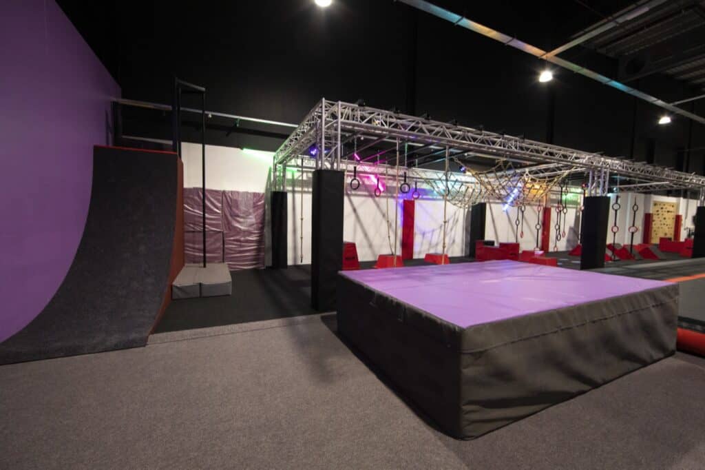 Climbing and obstacle course setup in a gym or training facility with various equipment, mats, and colourful lighting for functional fitness or ninja warrior training.