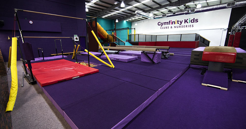 Brightly coloured indoor children's gymnastics play area featuring foam blocks, mats, and climbing equipment at Gymfinity Kids, a popular kids' clubs and nurseries facility in the UK.