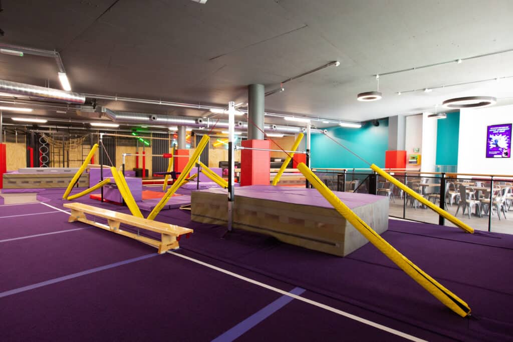 Climbing gym with colourful padded obstacles, ropes, and ramps designed for indoor parkour, training, and play in a vibrant, modern facility. Perfect for all ages seeking active fun and skill development.