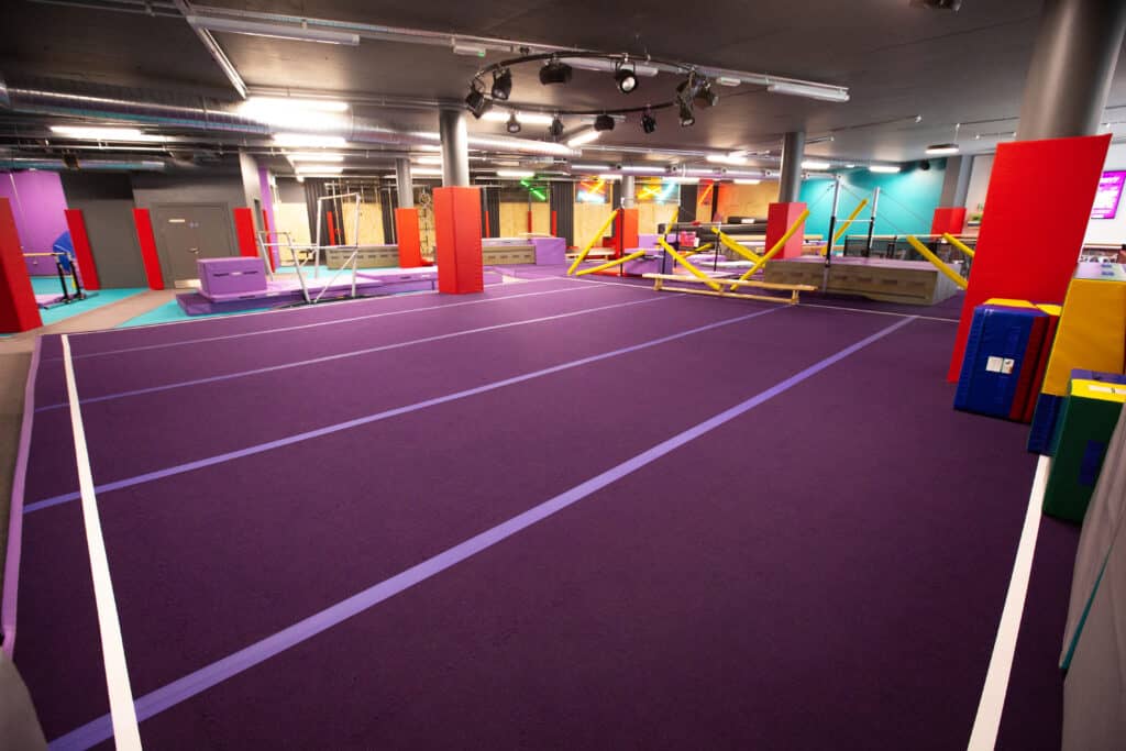 Bright indoor parkour and ninja warrior training gym with purple padded floors, colourful obstacle courses, and climbing frames for kids and adults. Perfect for fitness, fun, and skill-building activities.