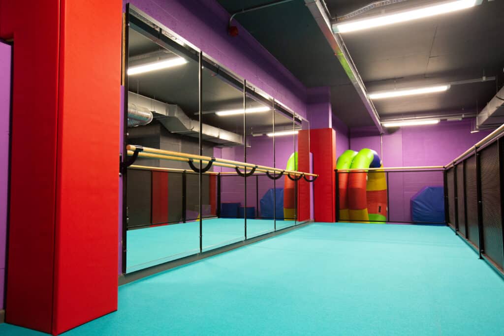 Brightly coloured indoor play area with purple walls, turquoise flooring, and soft play structures including a slide and climbing equipment, designed for children's recreation and physical activity.