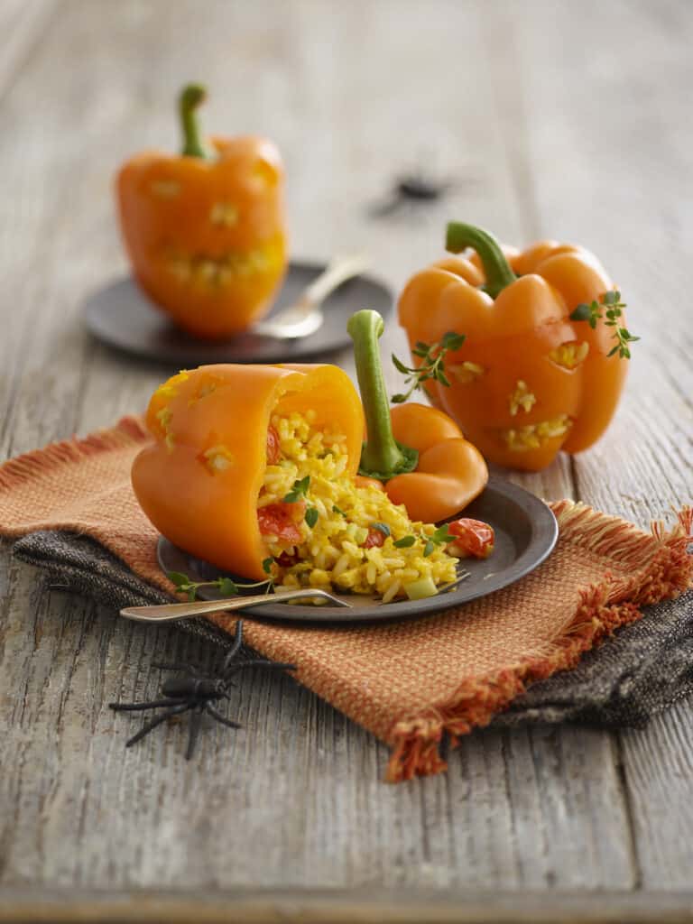 Golden stuffed bell peppers with rice, vegetables and herbs on a rustic wooden table, tasty and colourful ingredient-filled dish.