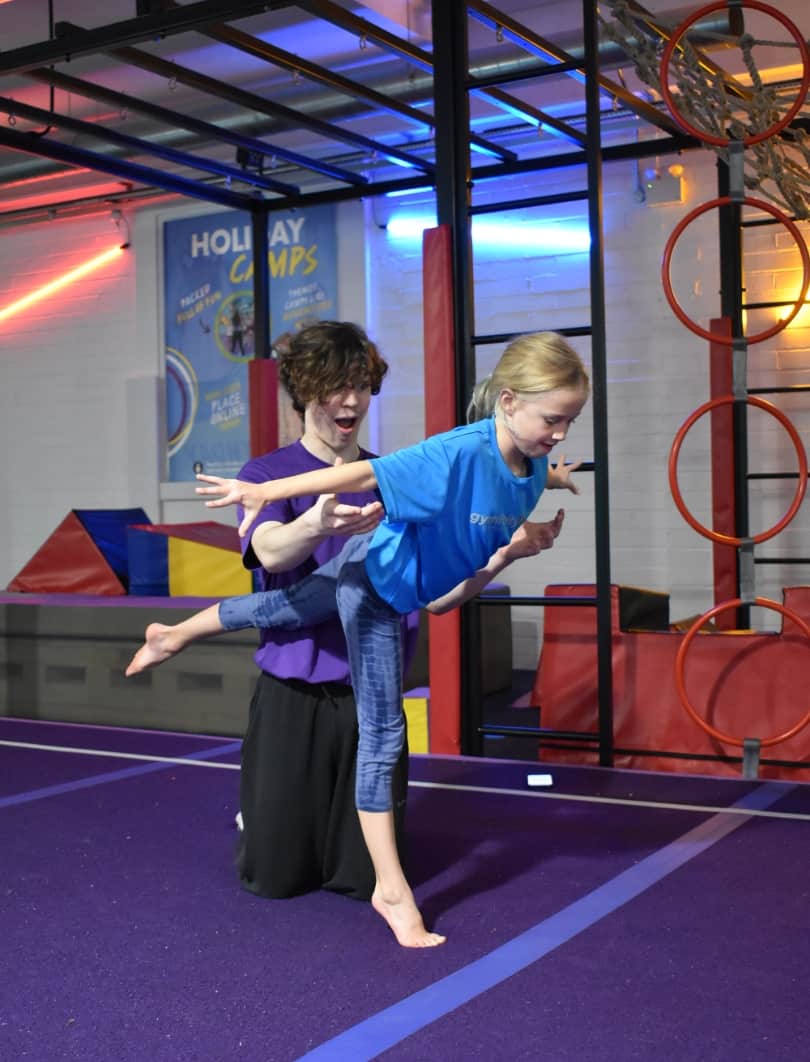 Children enjoying gymnastics activity in an indoor play area with colourful lighting and equipment.