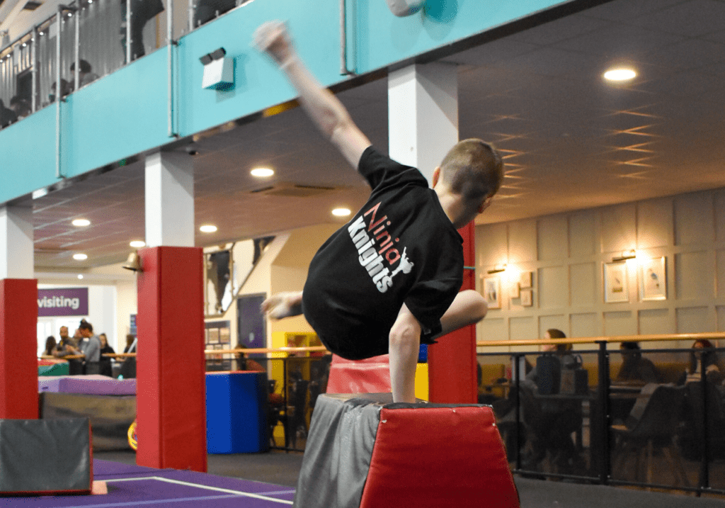 Boy performing handstand on padded mat in indoor gymnastics facility.