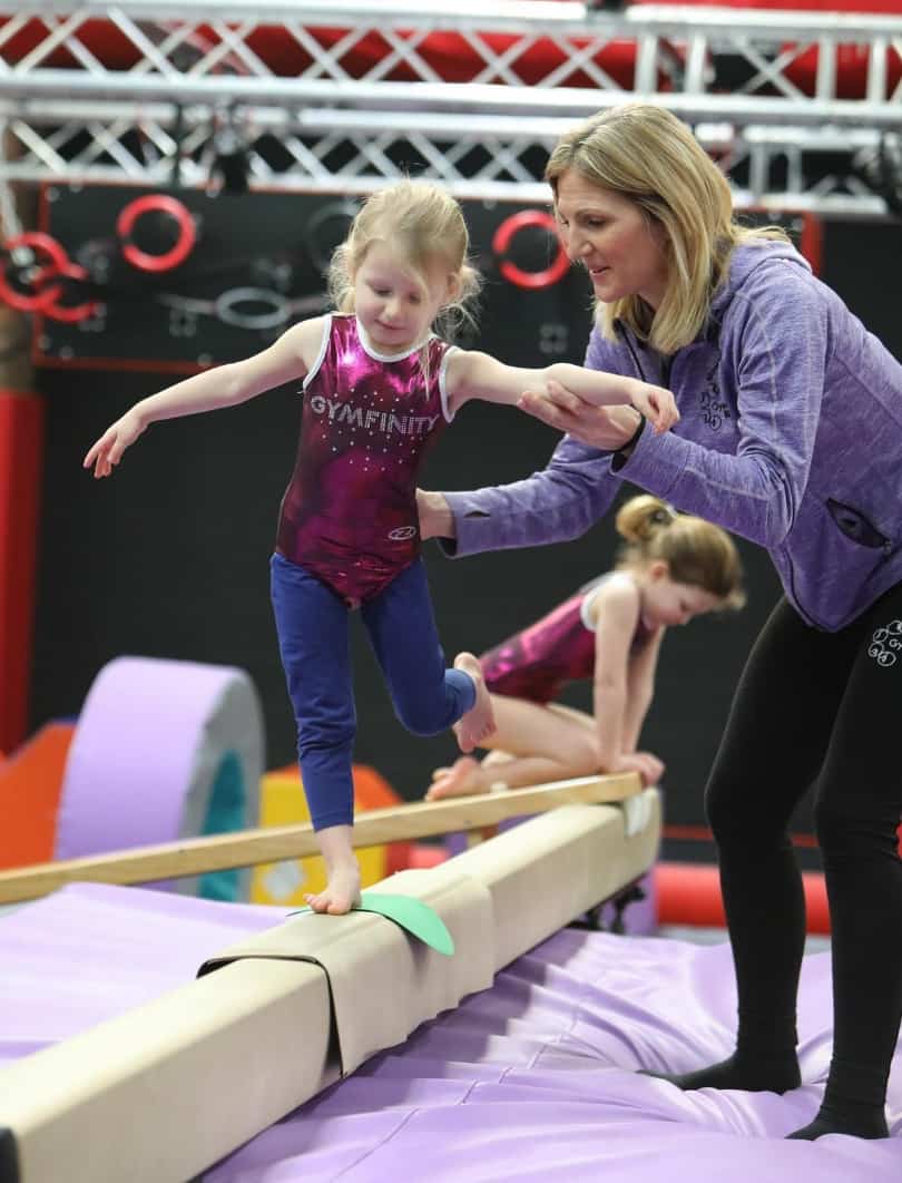 A girl practicing gymnastics on a balance beam with her coach's guidance during a training session.