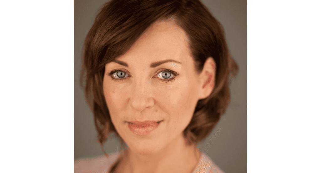 Girl doing a fitness workout on stage with audience members nearby during a lively event in a gym or community centre, with a green and red decorated background.
