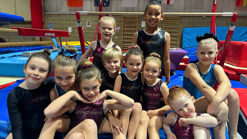Gymnastics team of young girls smiling at the camera in a gymnastics gym.
