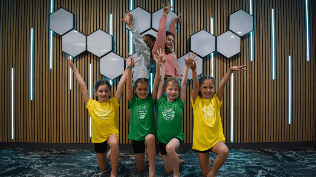 Children doing gymnastic exercise indoors, kids in colorful sportswear participating in a fitness activity, fun, energetic, and inclusive environment in a modern gym or sports centre, smiling and engaging in physical activity, learning teamwork and fitness.