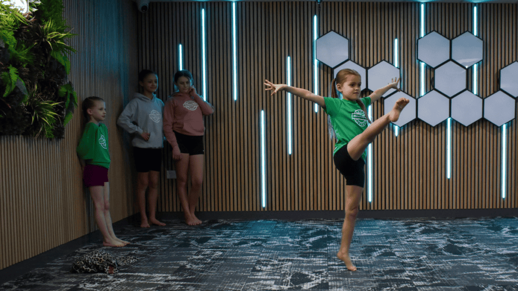 Dancer girl practicing dance move indoor with friends in background and modern decor.